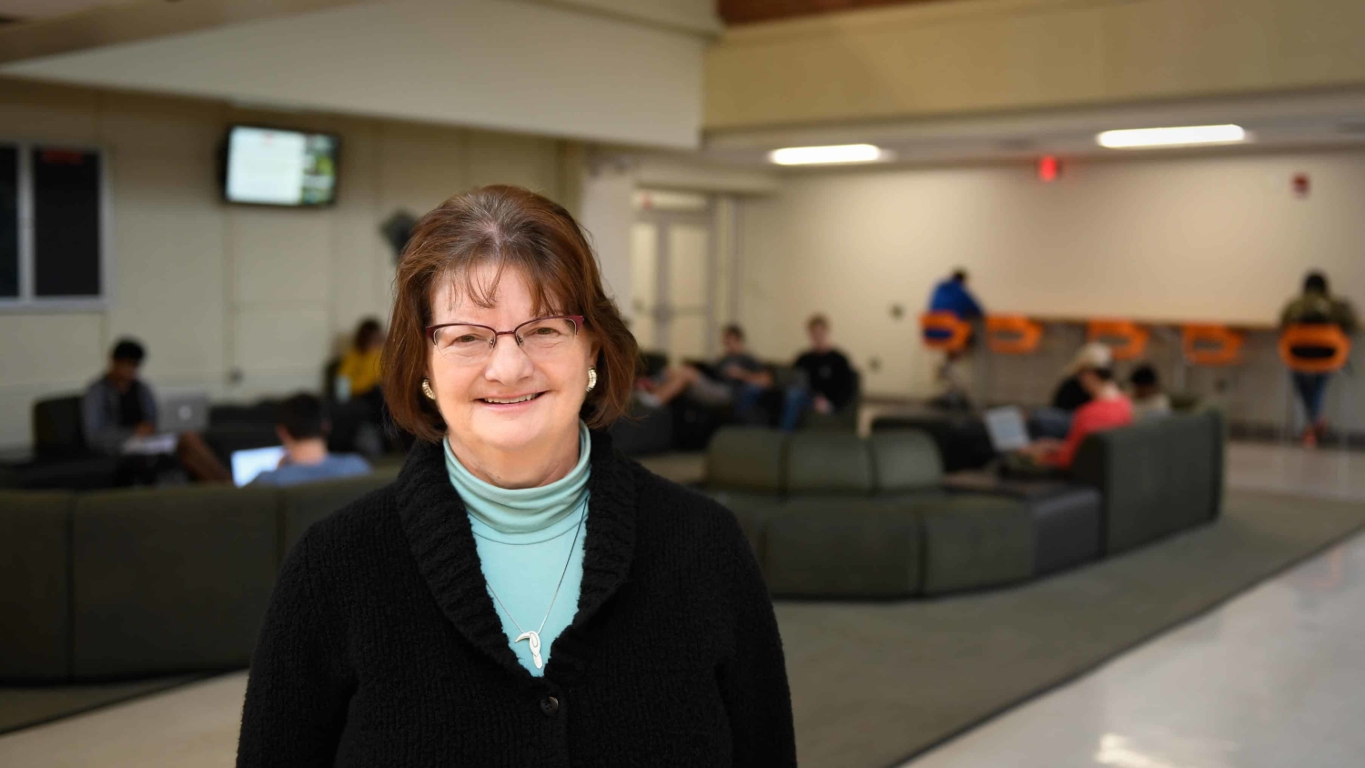 Statistics alumna Nancy Ridenhour in the commons area in Cox Hall with students working in the background