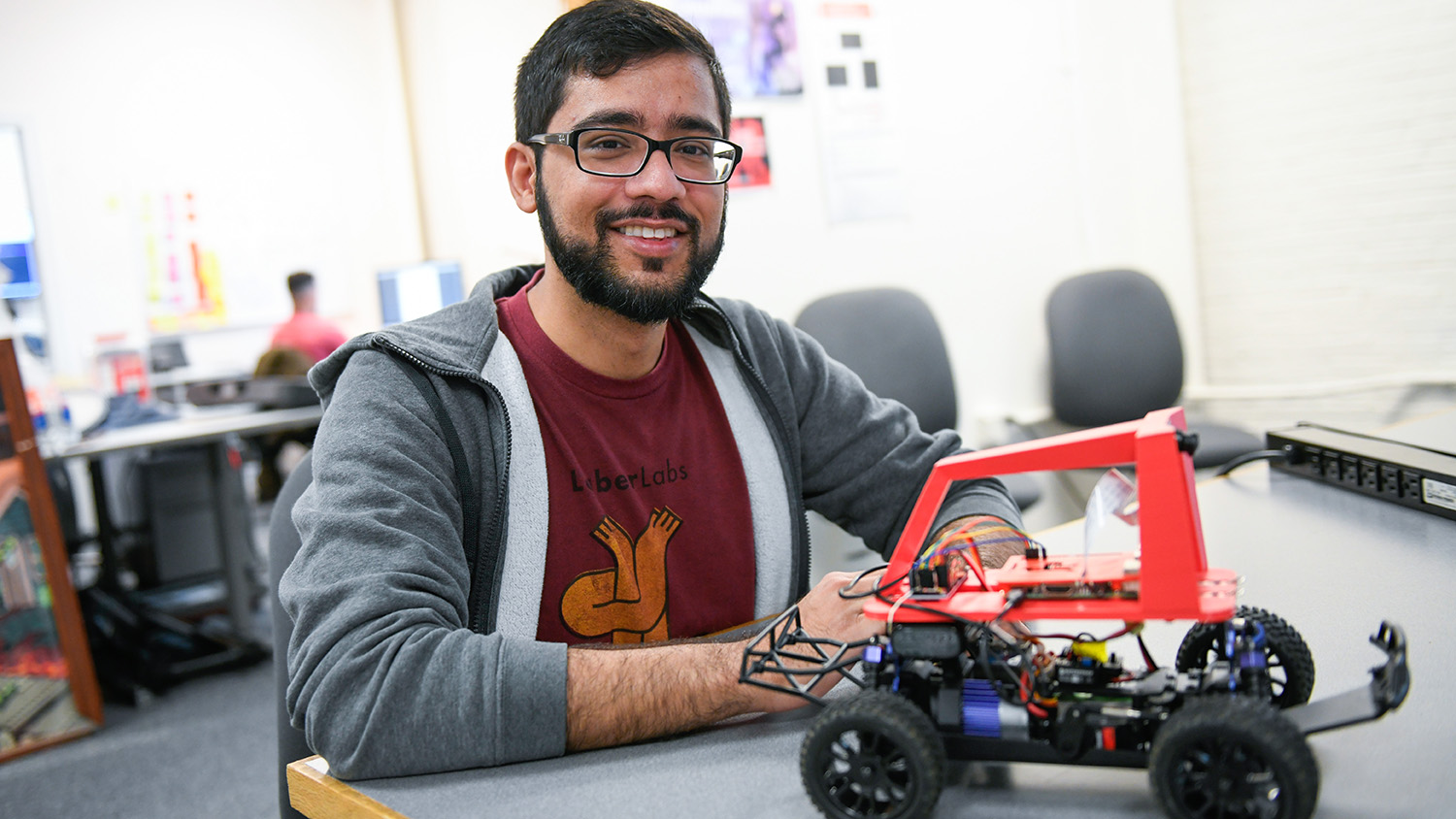 A male student sits at a table with a robotic car in front of him