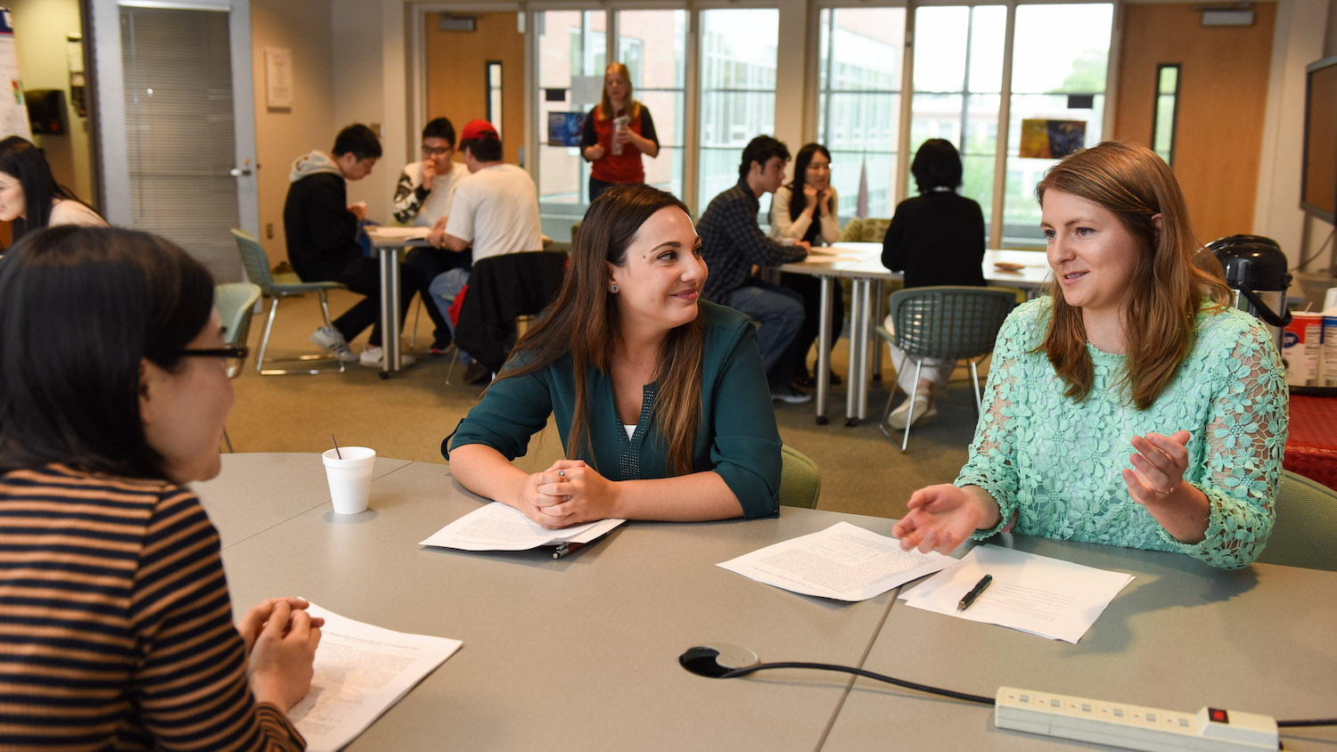 Students and faculty discuss research around a table in a common room